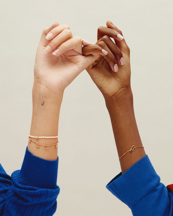 two hands are holding each other with their fingers in the air and one is wearing a gold bracelet