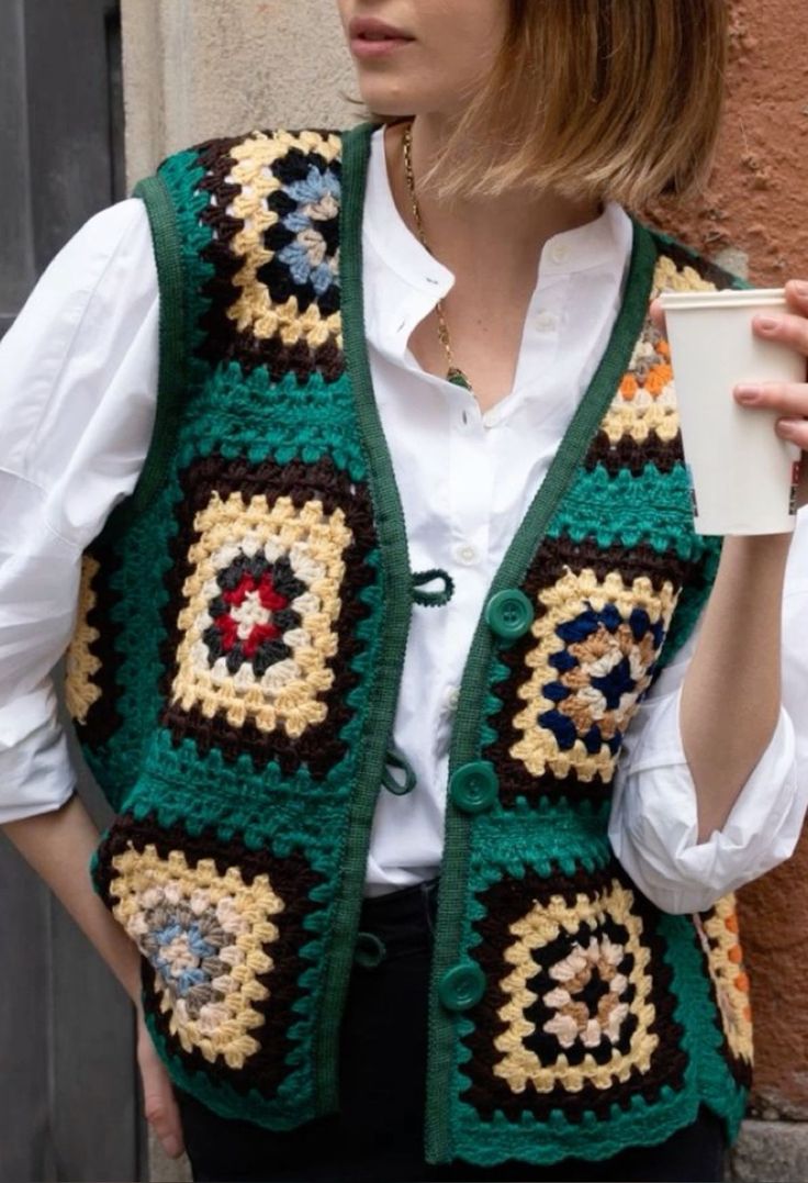 a woman holding a cup and wearing a crocheted vest