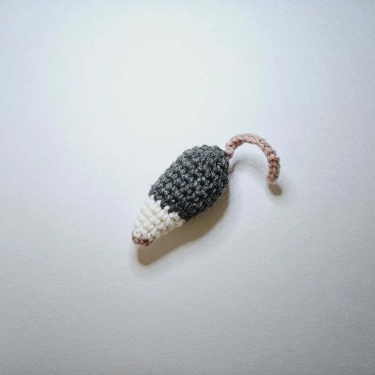 a crocheted toy mouse hanging from a string on a white wall with a gray and white background