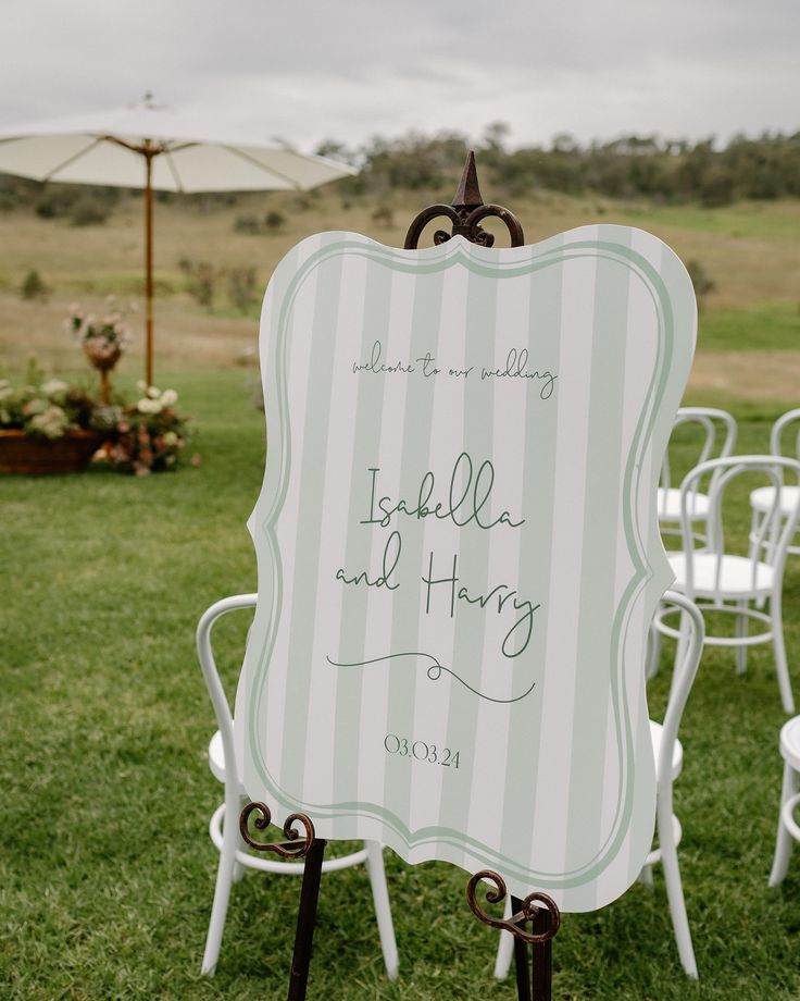 a sign that is sitting in the grass near some chairs and an umbrella with writing on it