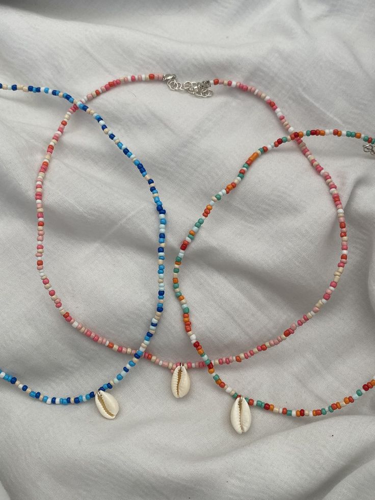 two necklaces with shells and beads on a white sheet