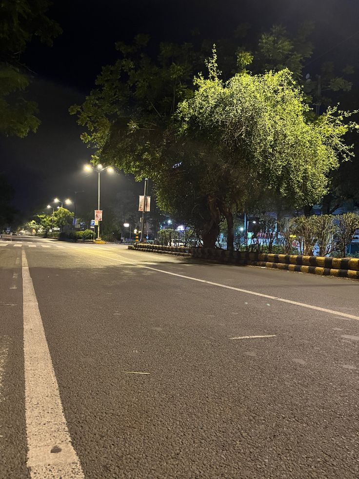 an empty street at night with no cars or people on the road and trees in the background