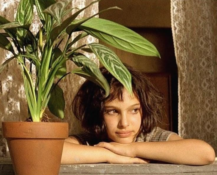 a woman sitting next to a potted plant on top of a window sill