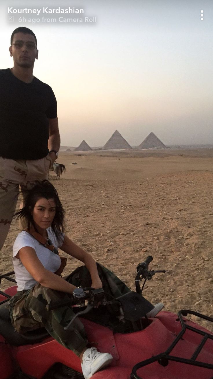 two people standing next to each other on an atv in front of the pyramids