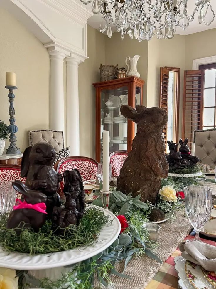 a dining room table set for christmas with bunny figurines and greenery on it