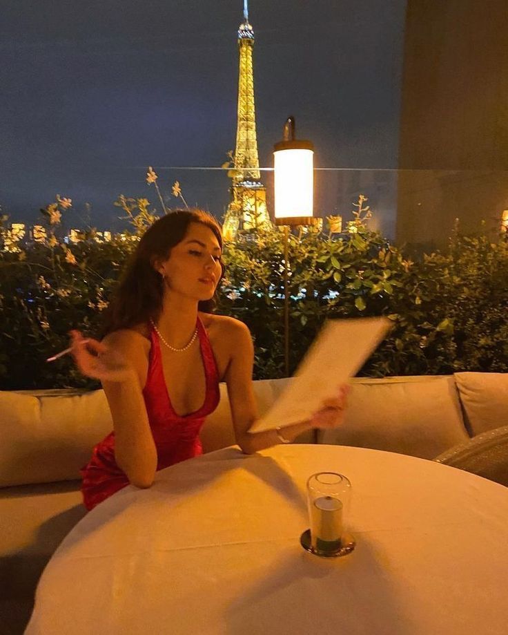 a woman sitting at a table in front of the eiffel tower reading a piece of paper