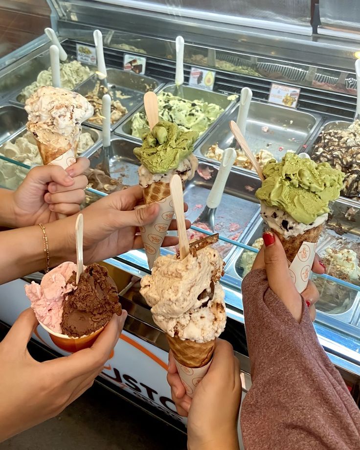 several people holding ice cream cones in front of an ice cream display case with scoops