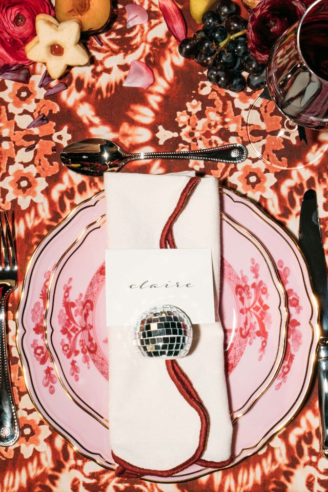 a place setting with napkins and silverware on a floral table cloth, surrounded by flowers