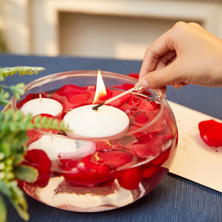 a person lighting a candle in a bowl filled with flowers