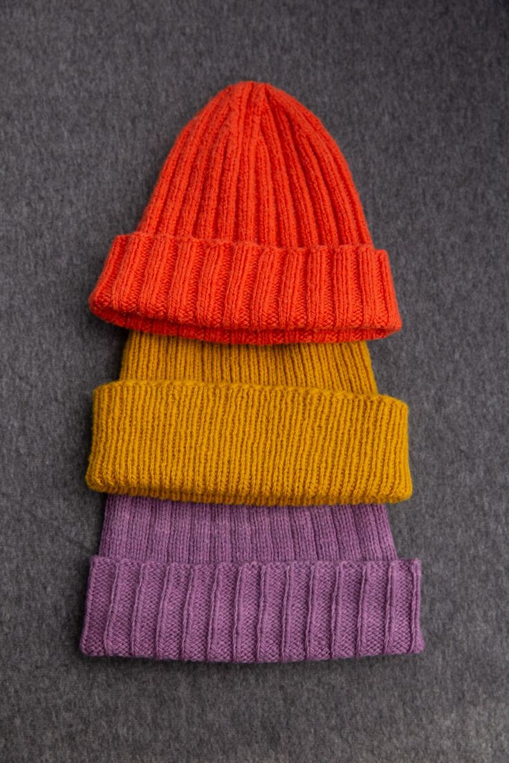 three different colored knitted hats sitting next to each other on top of a gray surface