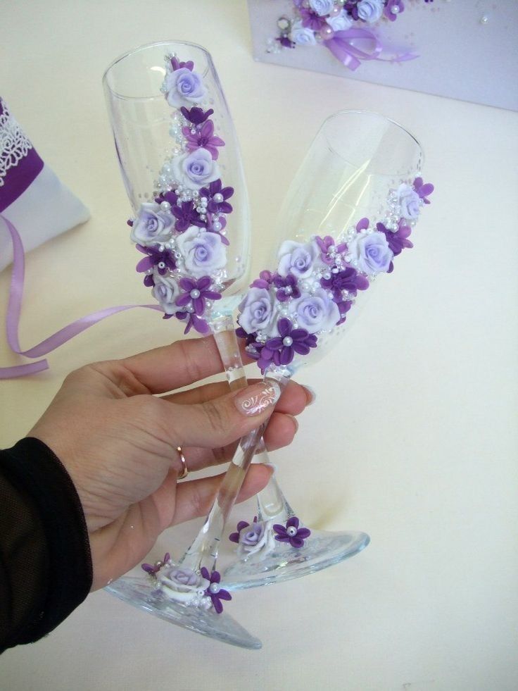 a hand holding two wine glasses with purple flowers on them and ribbons around the rims