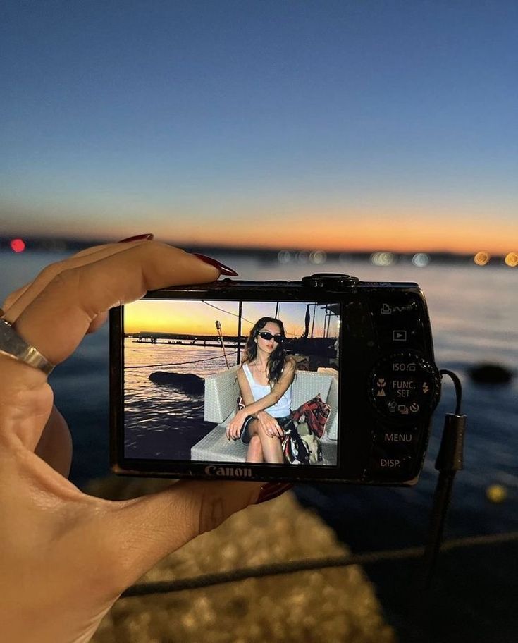 a person holding up a camera to take a photo on the beach at night time