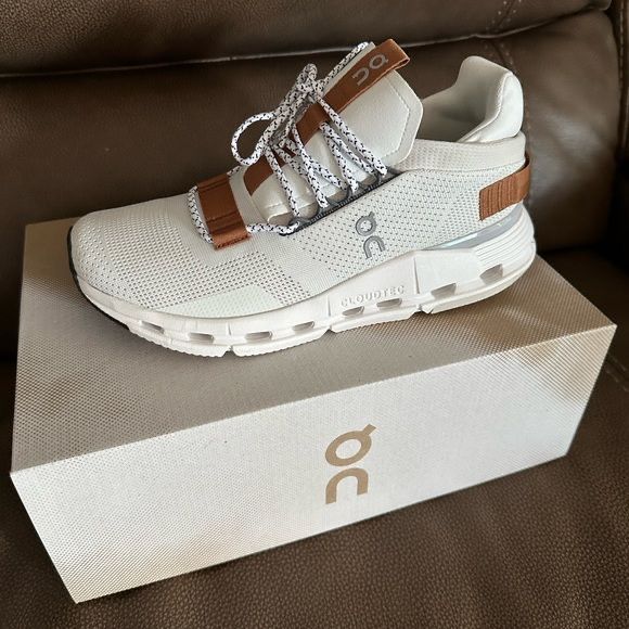 a pair of white sneakers sitting on top of a box next to a brown couch