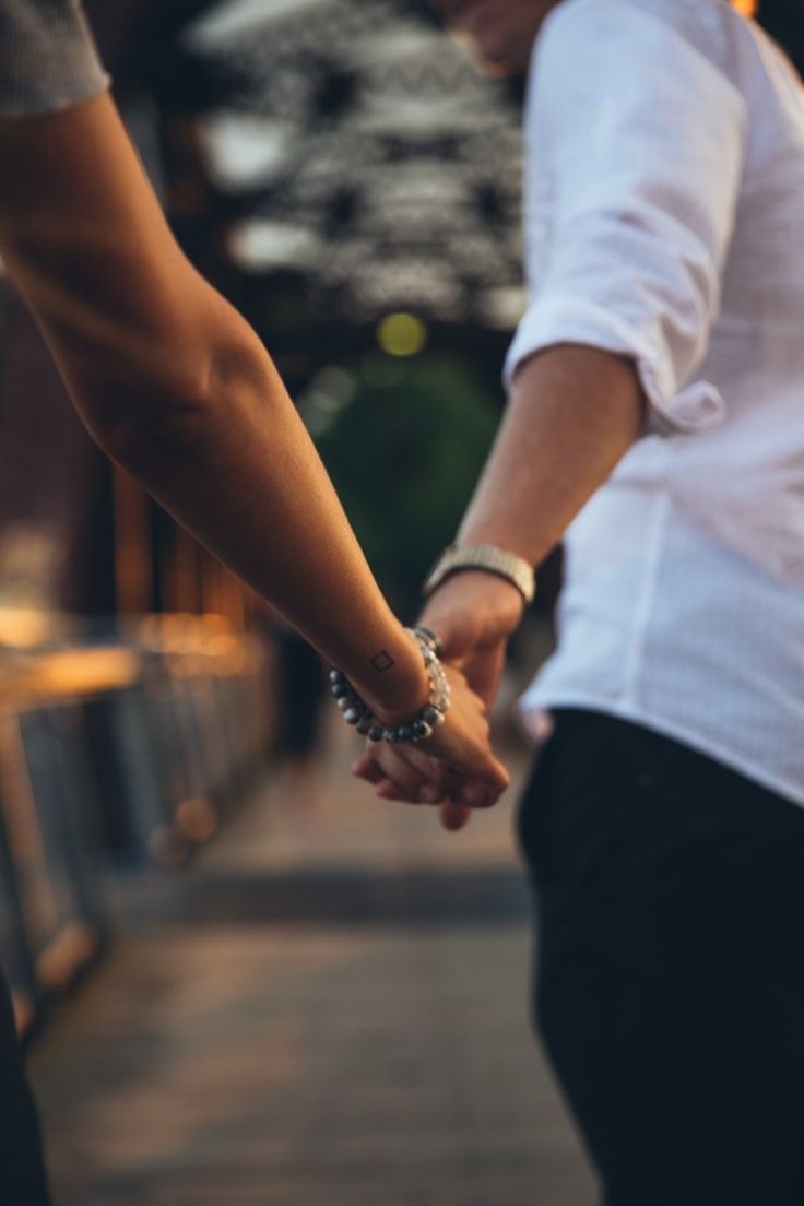 two people holding hands while walking down the street