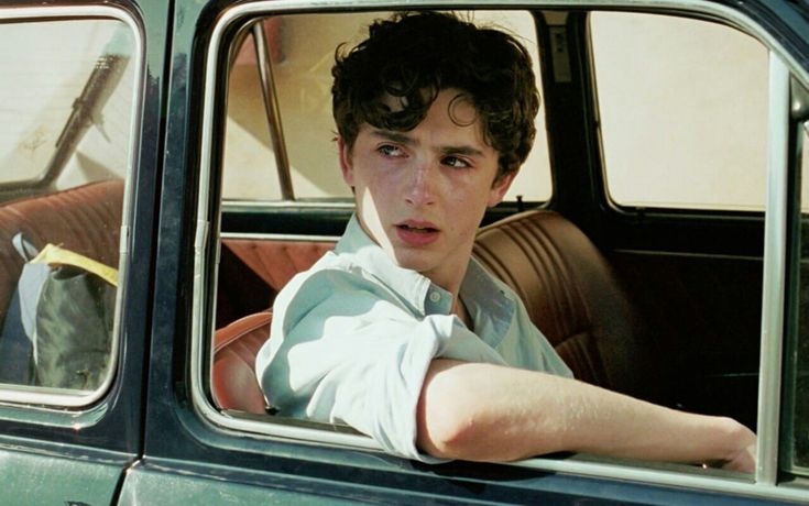 a young man sitting in the driver's seat of a car looking out the window