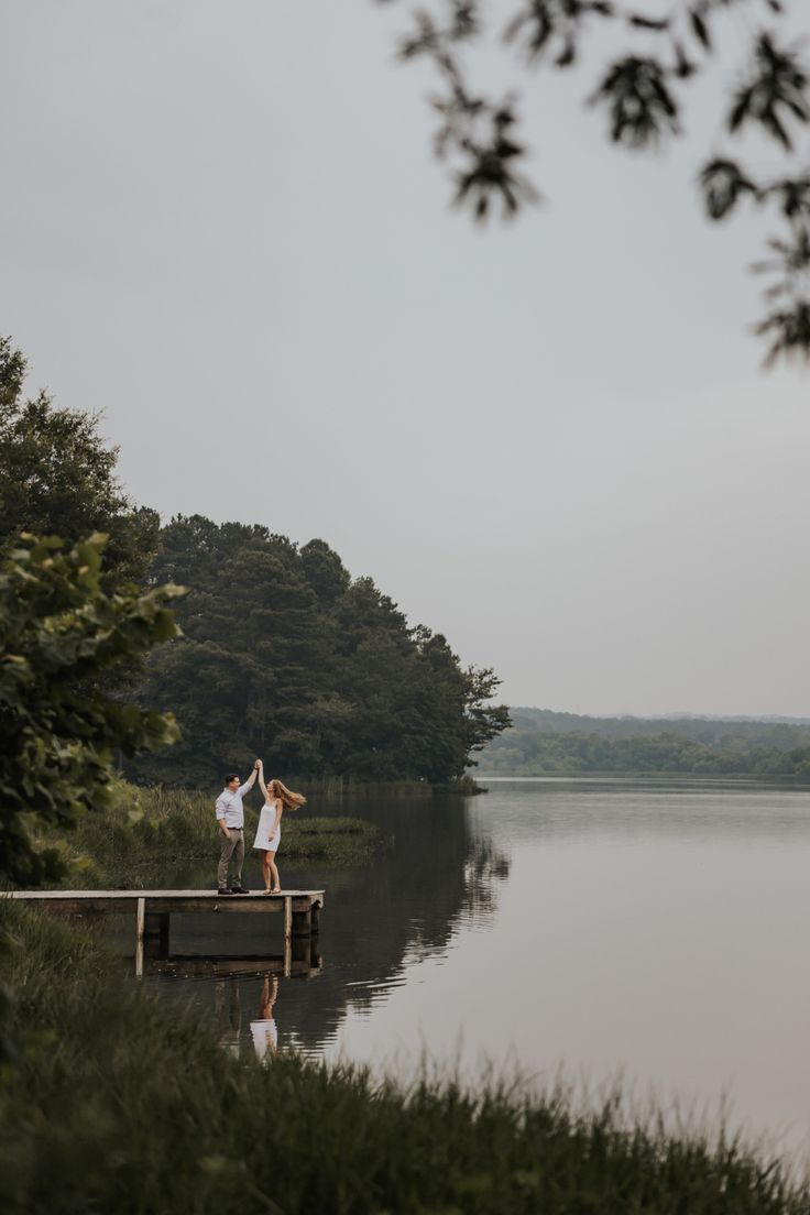 two people are standing on a dock by the water with their arms in the air