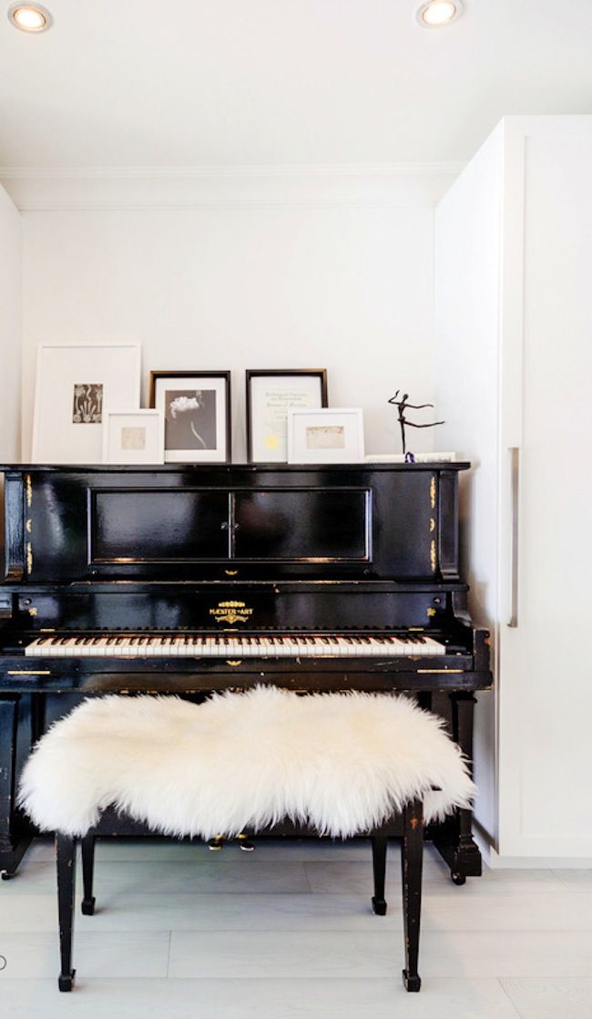 a black piano with a white bench in front of it and pictures on the wall