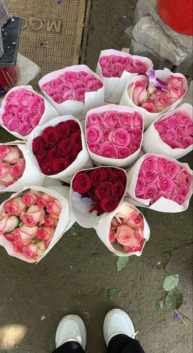 a person standing next to a bunch of roses in white paper bags on the ground