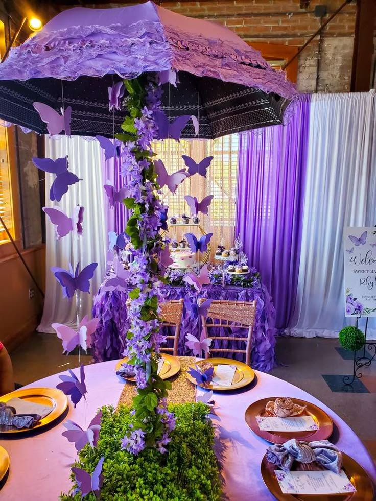 the table is set with purple butterflies and greenery for an outdoor wedding or bridal party