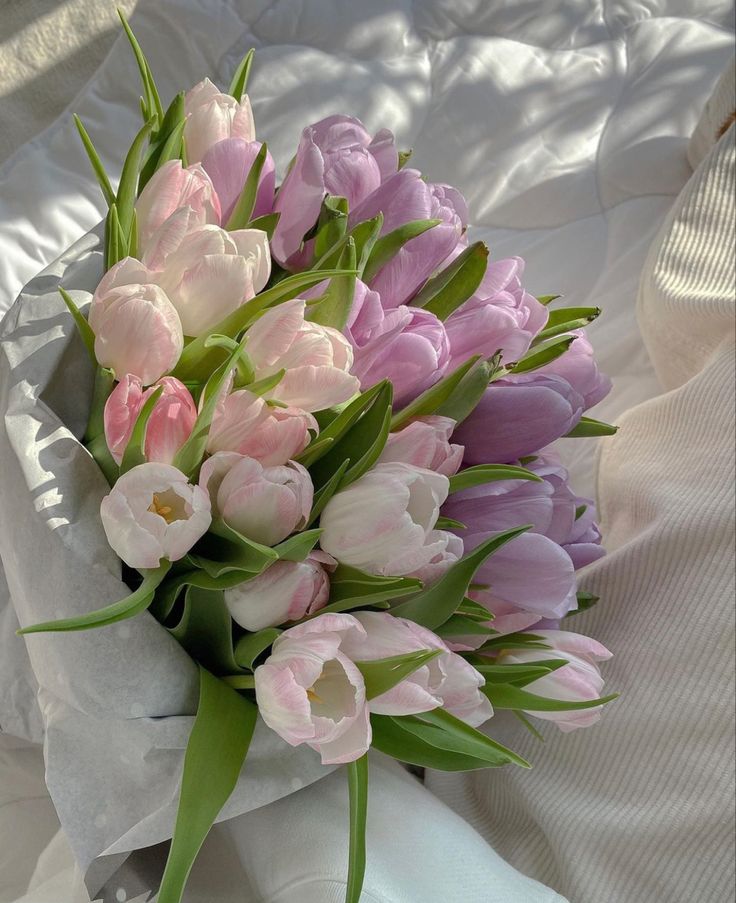 a bouquet of pink and white tulips sitting on top of a bed sheet