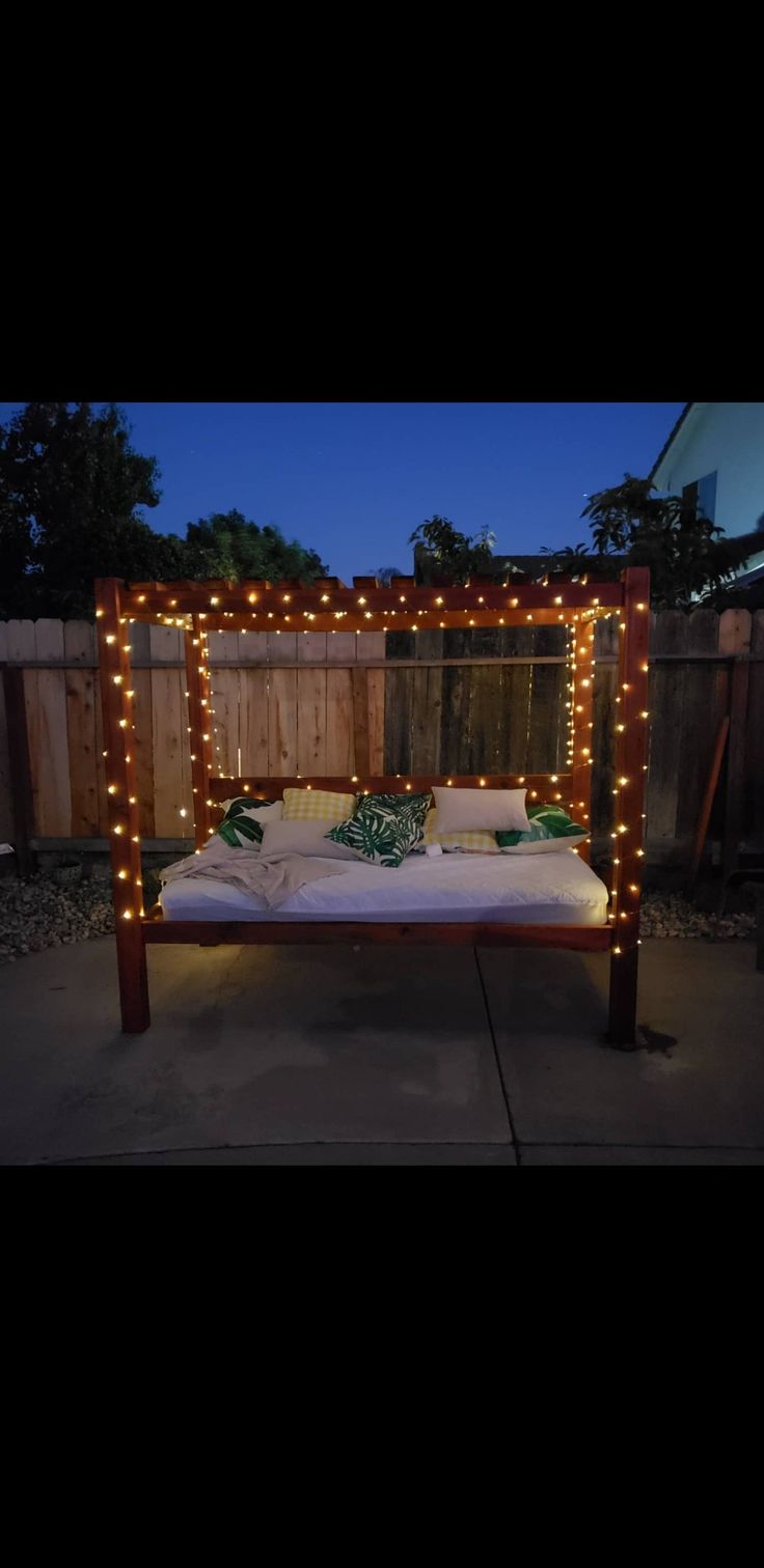 a bed with lights on it in the middle of a yard at night, next to a fence