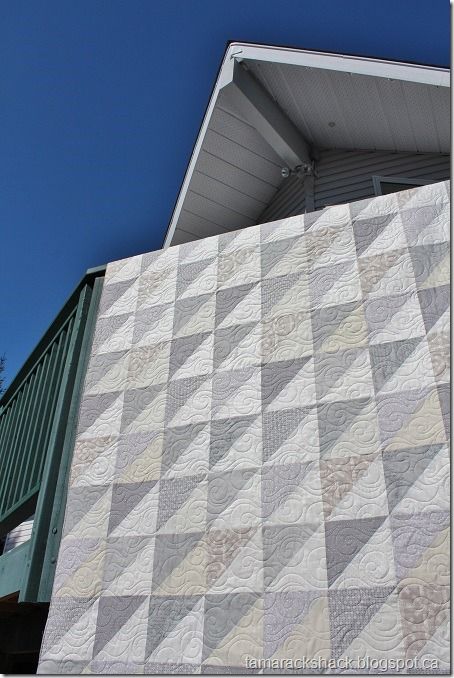 a white and grey quilt on the side of a building with blue sky in background