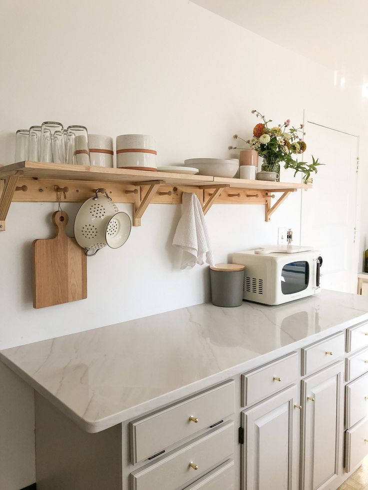 a kitchen with white cabinets and wooden shelves on the wall above it is a microwave