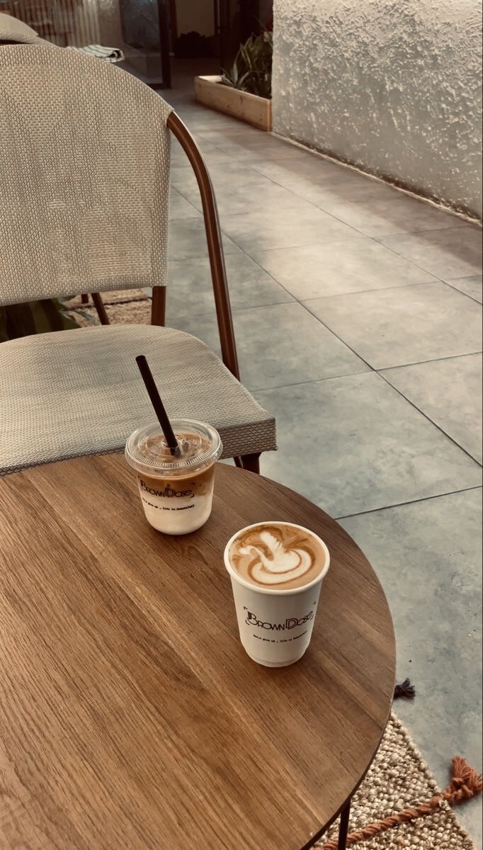 two cups of coffee sitting on top of a wooden table next to a white chair