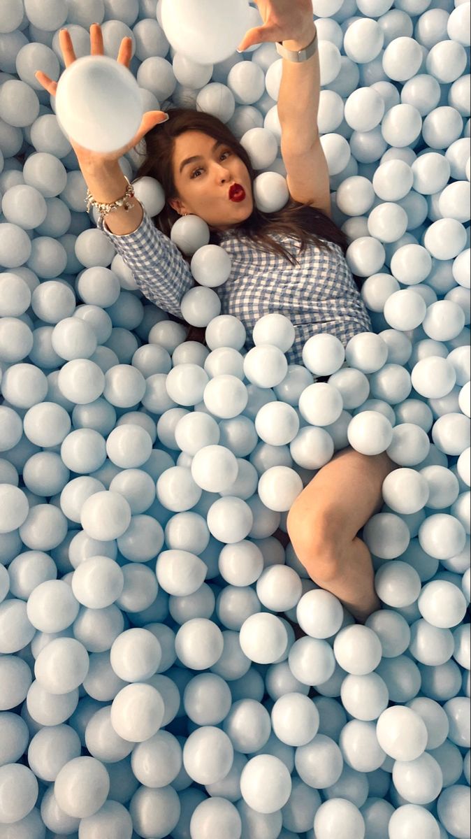 a woman laying in a ball pool with balls all over her body and hands above her head