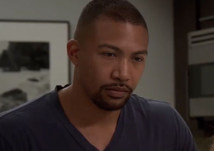 a close up of a person in a room with a microwave and cabinets behind him