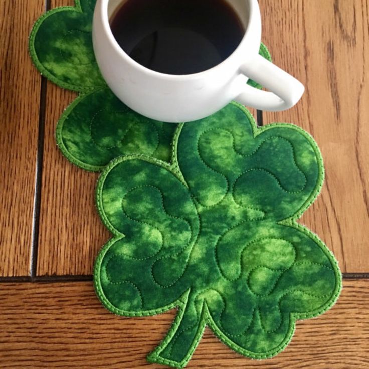 a cup of coffee sitting on top of a wooden table next to a shamrock coaster