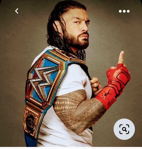 a man with long hair and tattoos wearing a wrestling outfit pointing to the left side