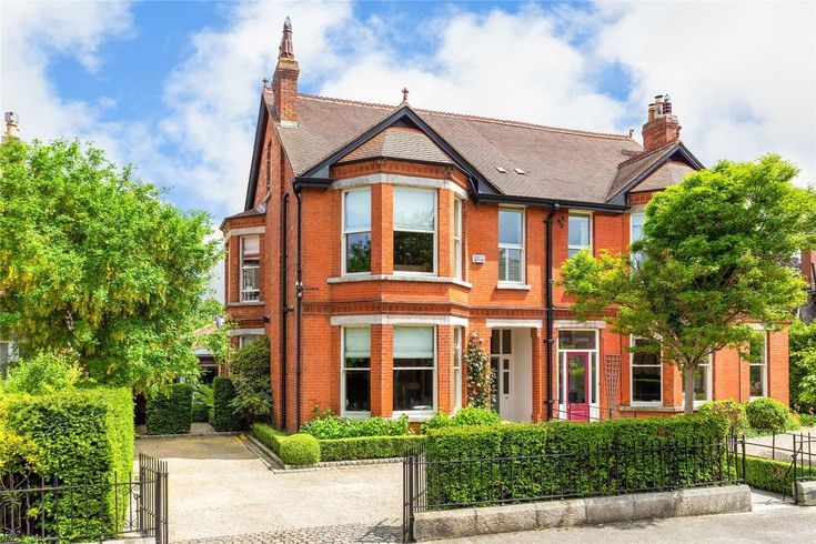 a large red brick house surrounded by trees and hedges on a sunny day with blue sky in the background