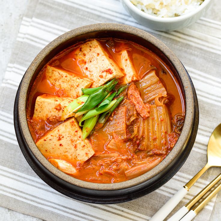 a bowl filled with tofu and vegetables on top of a table next to rice