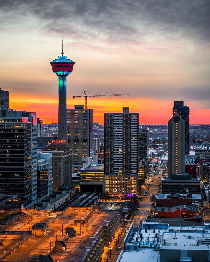 a city skyline with tall buildings and a colorful tower in the background at sunset or dawn