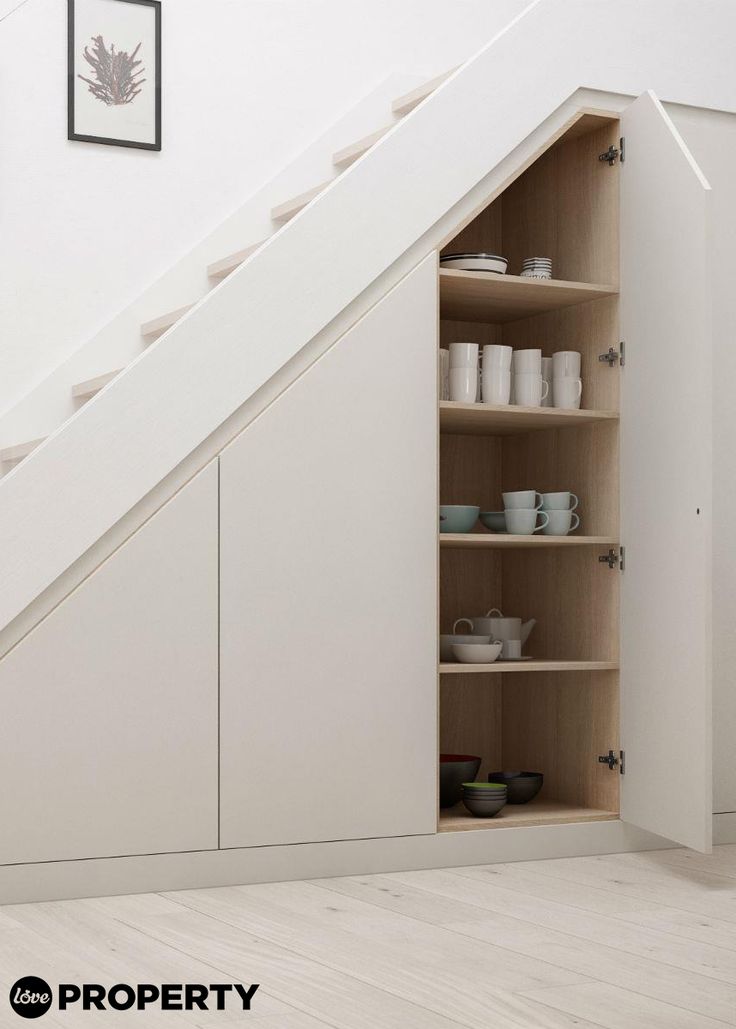 an open cabinet under the stairs in a room with white walls and wooden floors, filled with dishes