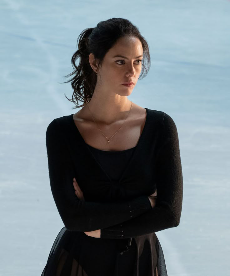 a woman standing with her arms crossed in front of the camera, wearing a black dress