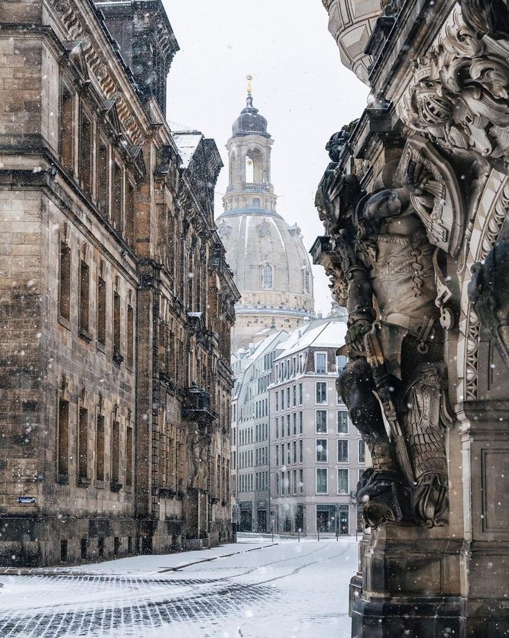 an old city street is covered in snow and has statues on the side of it