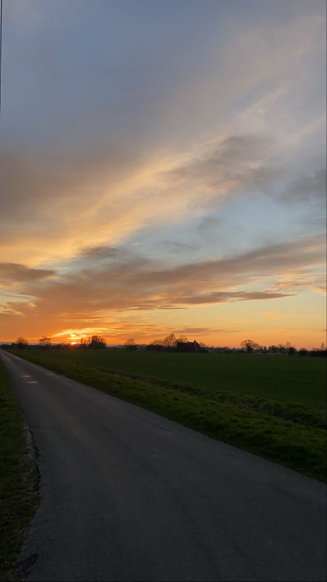 the sun is setting over an empty country road