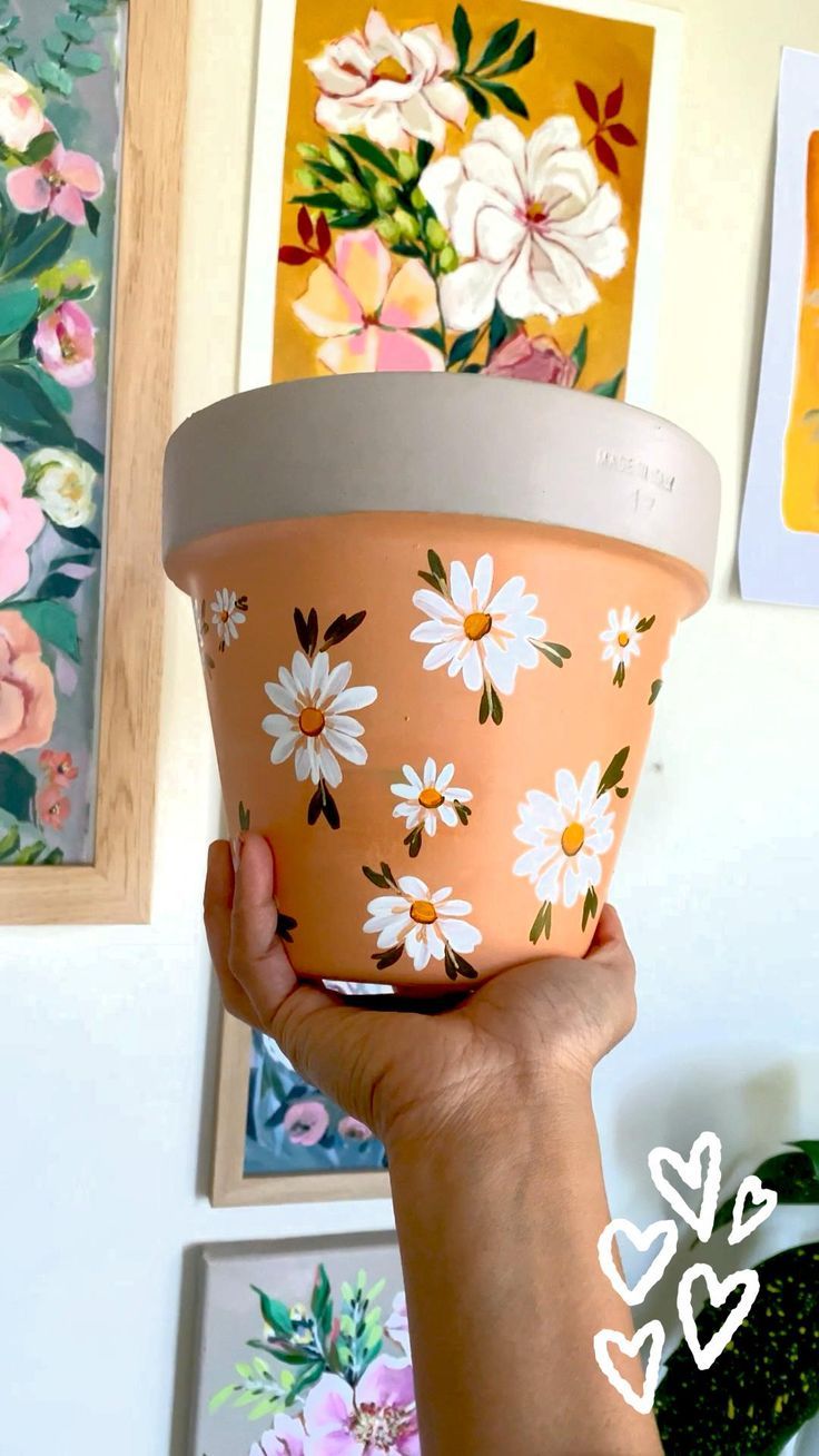 a person holding up a flower pot in front of some pictures on the wall behind them