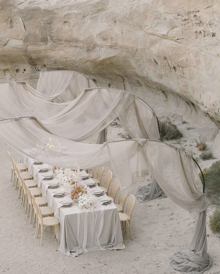 a table set up for an outdoor dinner in the desert with sheer draping