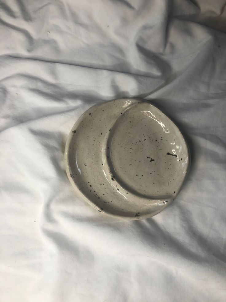 two white plates sitting on top of a bed next to each other with black speckles