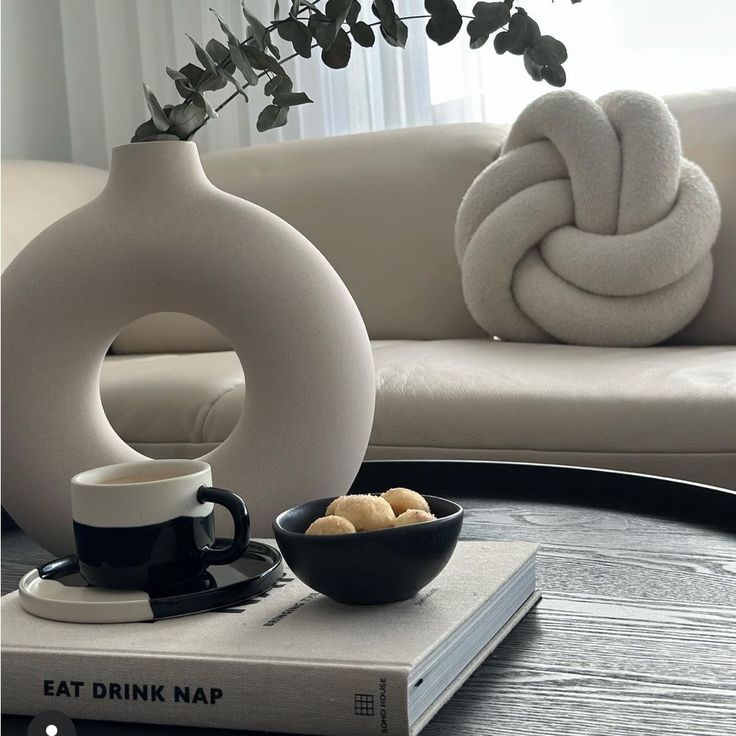 a coffee table topped with a vase filled with flowers next to a book and cup