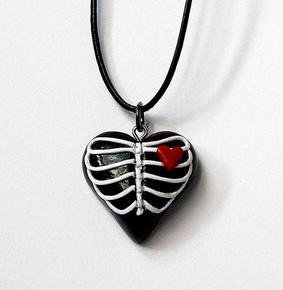 a black heart shaped pendant with a red heart on it's side and a skeleton in the middle