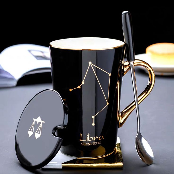 a black coffee mug sitting on top of a table next to a spoon and book