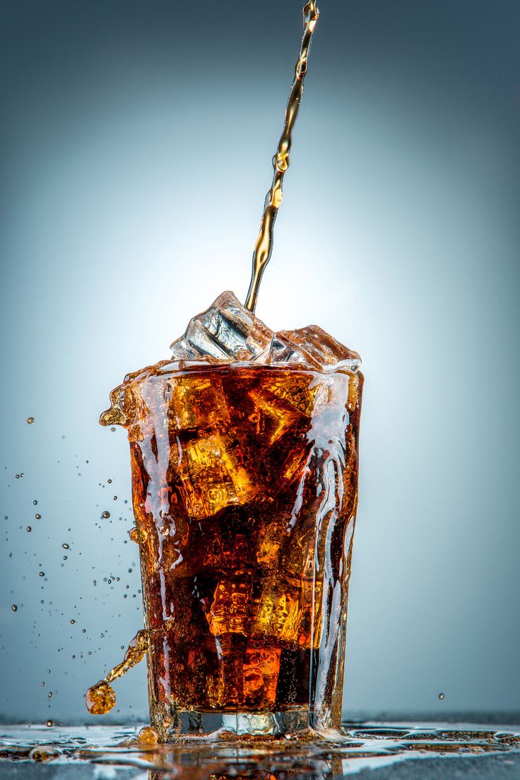 a glass filled with liquid and ice cubes on top of a table next to a blue background