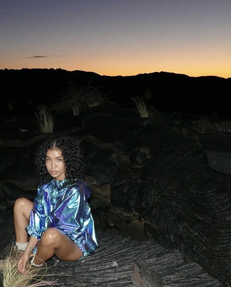 a woman sitting on top of a pile of dirt next to a forest at night