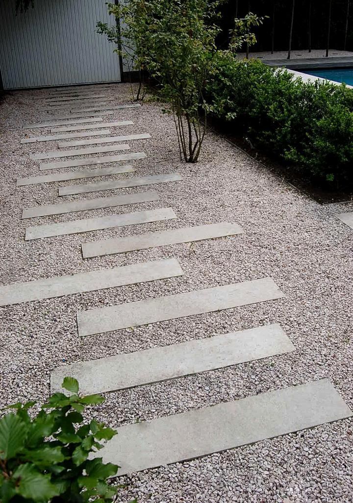 a stone path in the middle of a graveled area next to a swimming pool