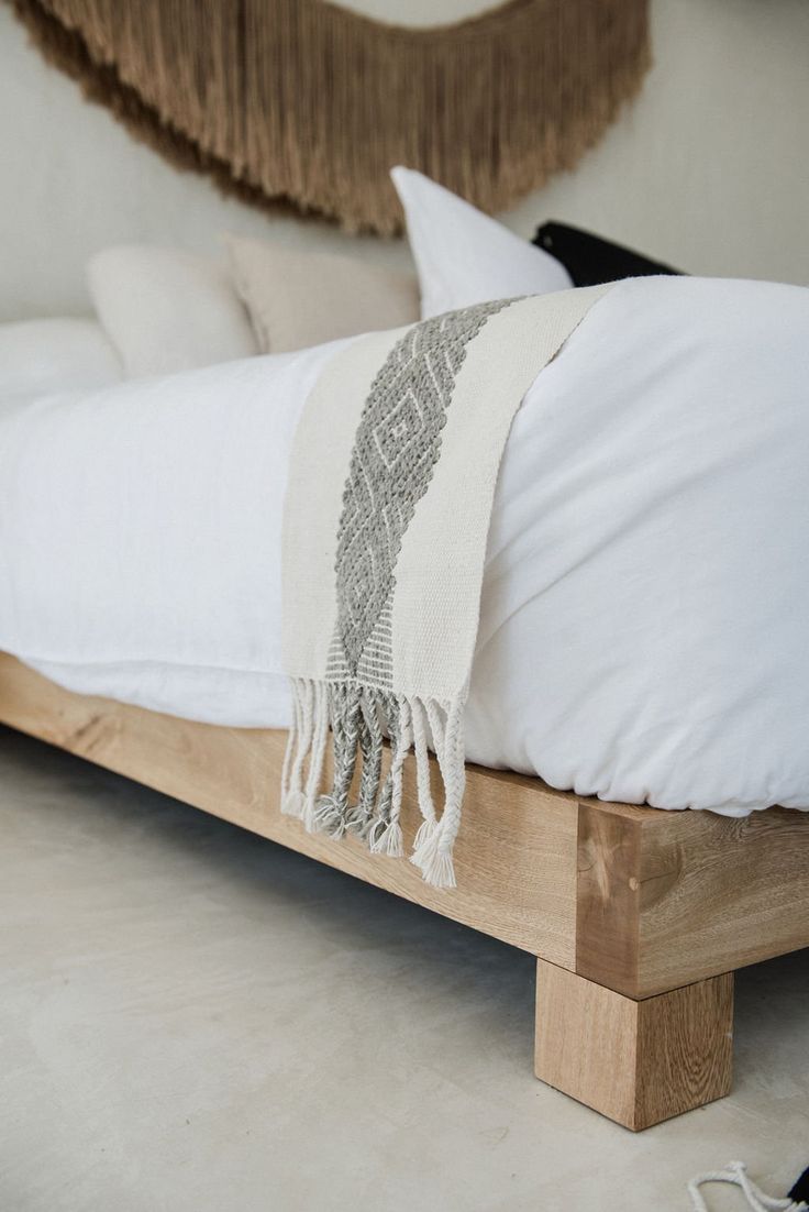 a bed with white pillows and a wooden frame on the bottom floor, in front of a large wall hanging