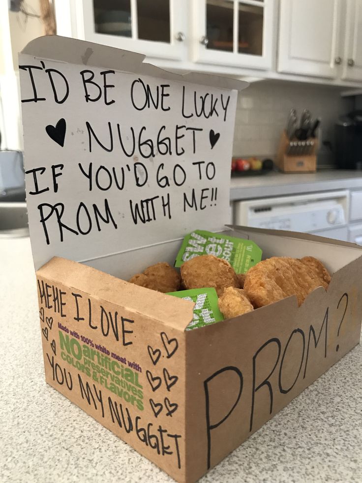 a box filled with donuts sitting on top of a counter next to a sign that says i'd be one lucky nugget if you'd go to prom